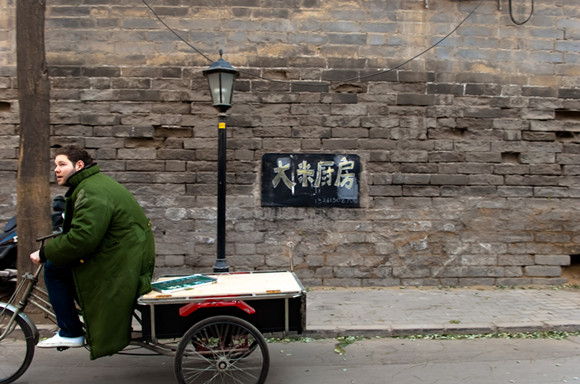 Jamie is wheeling his souped-up tricycle that serves as a mobile snack stand near Shichahai, a historic scenic area in Beijing, on Dec. 7, 2011 (Xinhua/Liu Jinhai)